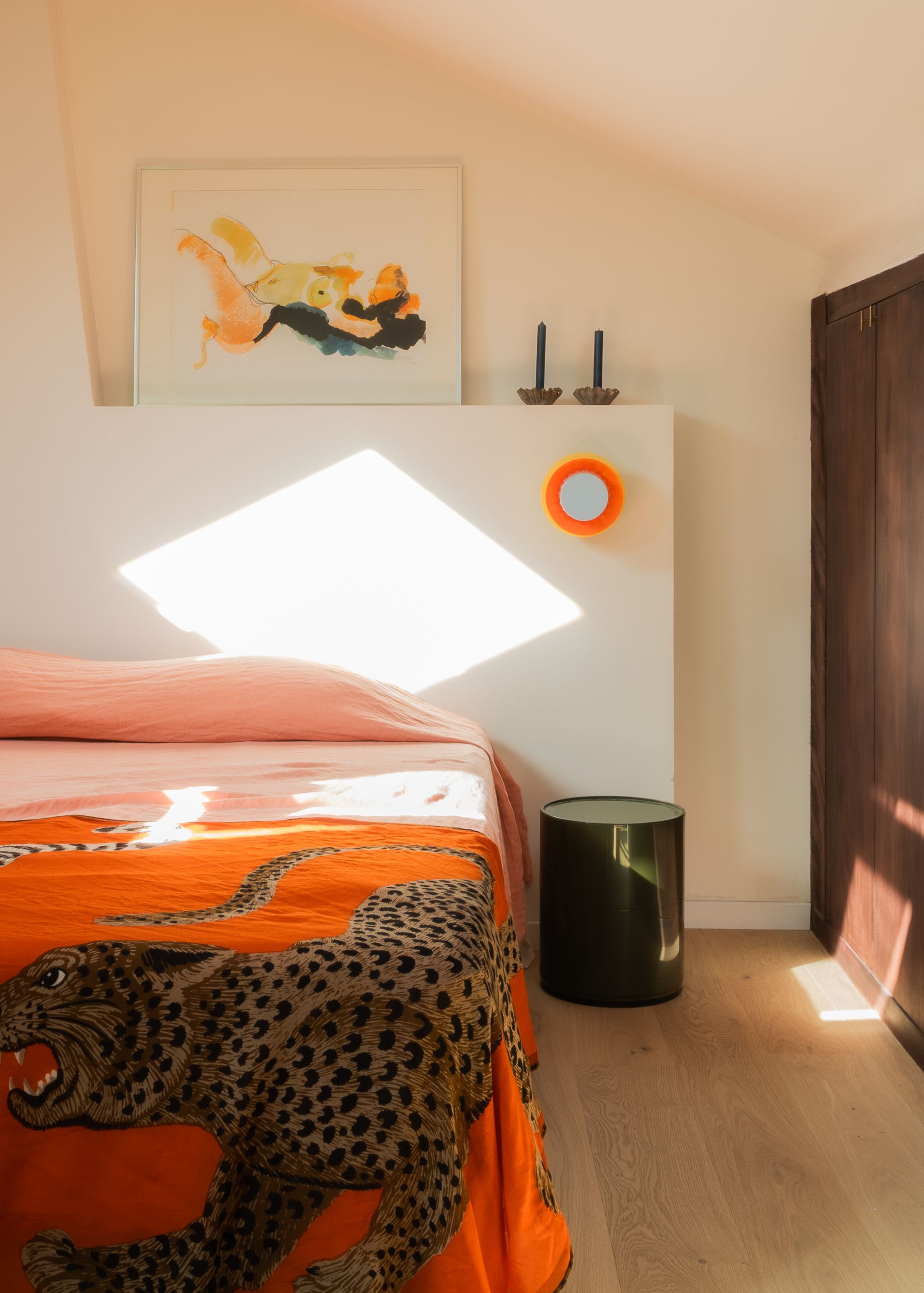 A bedroom with orange sheets, beige walls and a study hidden inside a wardrobe