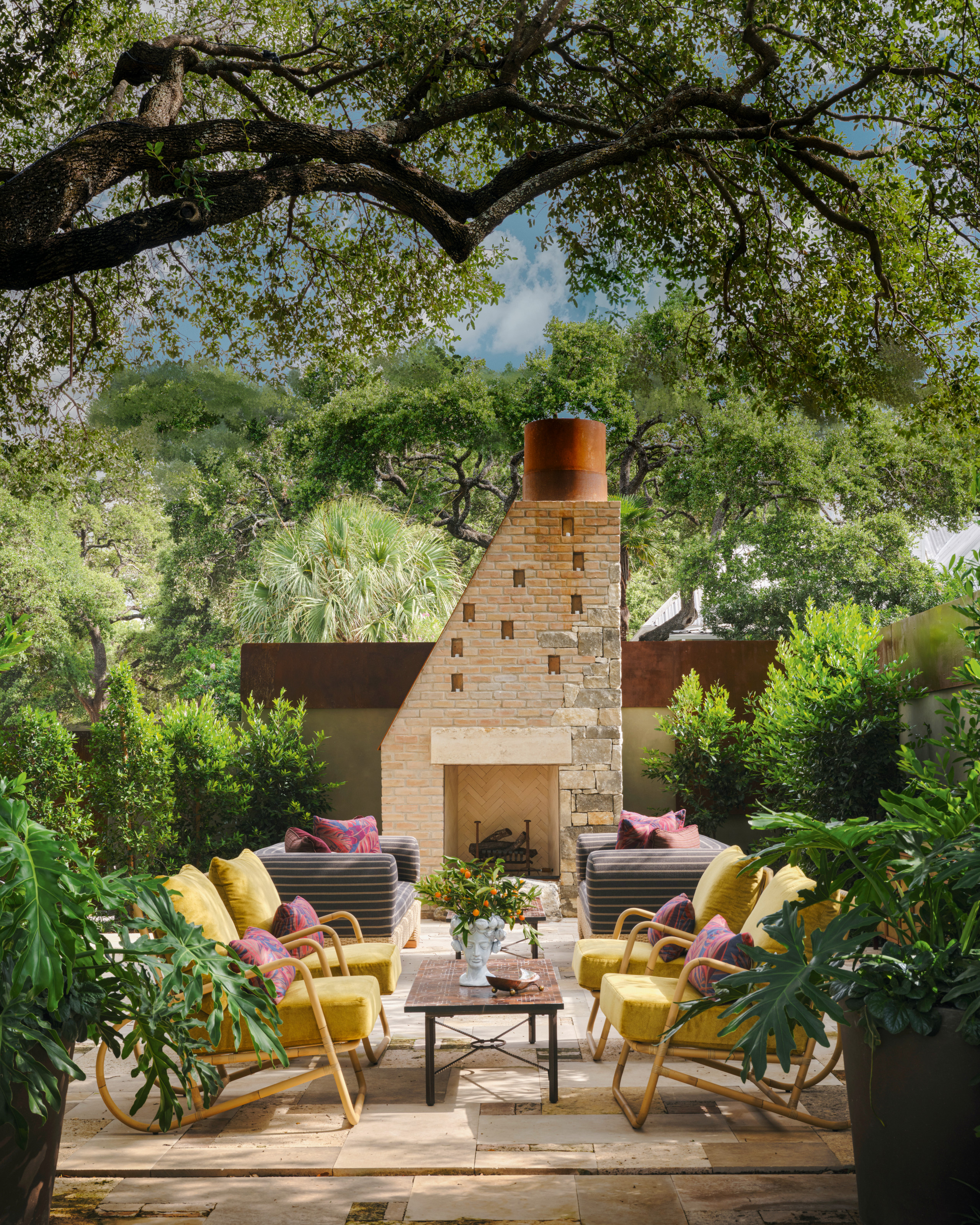 Garden with brick fireplace and chimney, yellow and cane armchairs, dark green and white striped armchairs, coffee table and abstract rug
