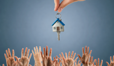 Hand holding a house key above a crowd of raised hands symbolising competition in the rental market