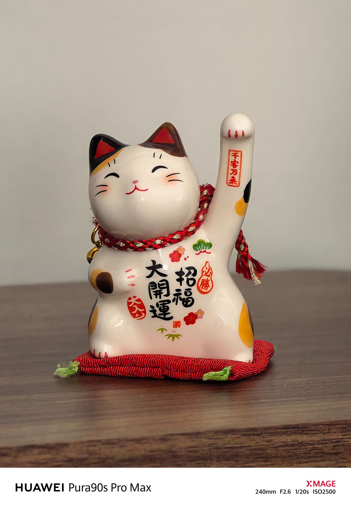 Close-up of a ceramic Japanese lucky cat with colorful markings, black lettering and a raised paw.