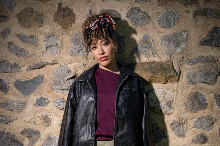 Emm_Serena_Sugden_02 (1) Casey Al-Shaqsy as Serena Sugden in Emmerdale, stood against a stone wall and wearing a black leather jacket.