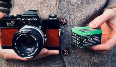 Person holding a vintage Minolta SR-T Super camera in one hand and a box of Fujifilm Neopan Acros 100 II black-and-white film in the other.