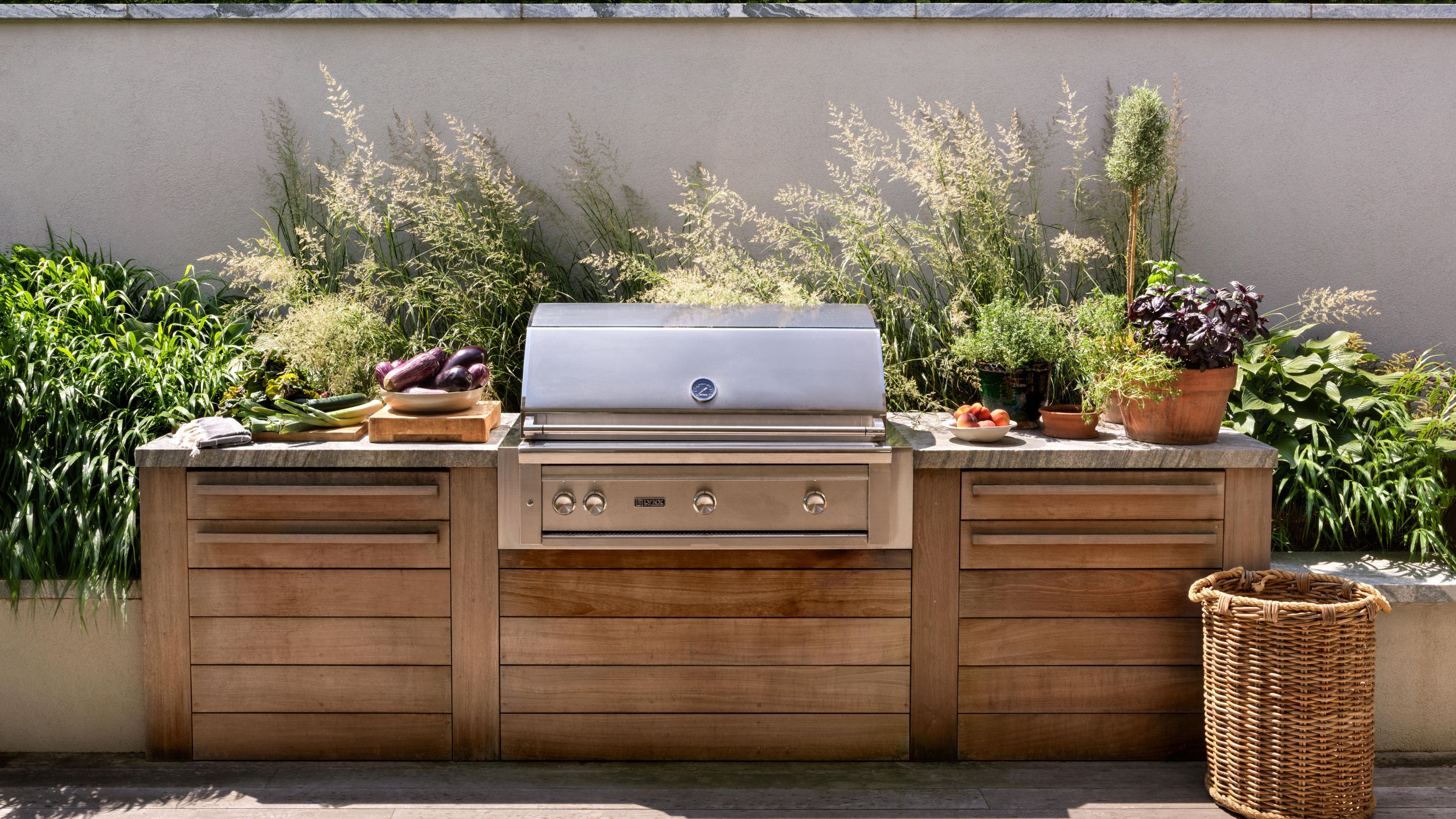 a wooden outdoor kitchen with bbq and grown planter of grasses and foliage