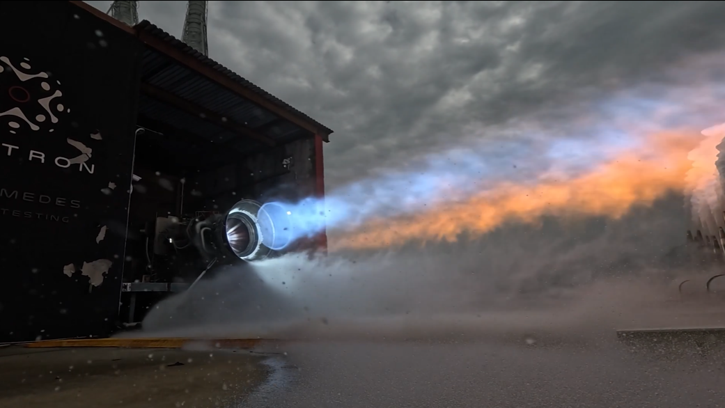 A rocket engine on a test stand blasts blue and orange flame.