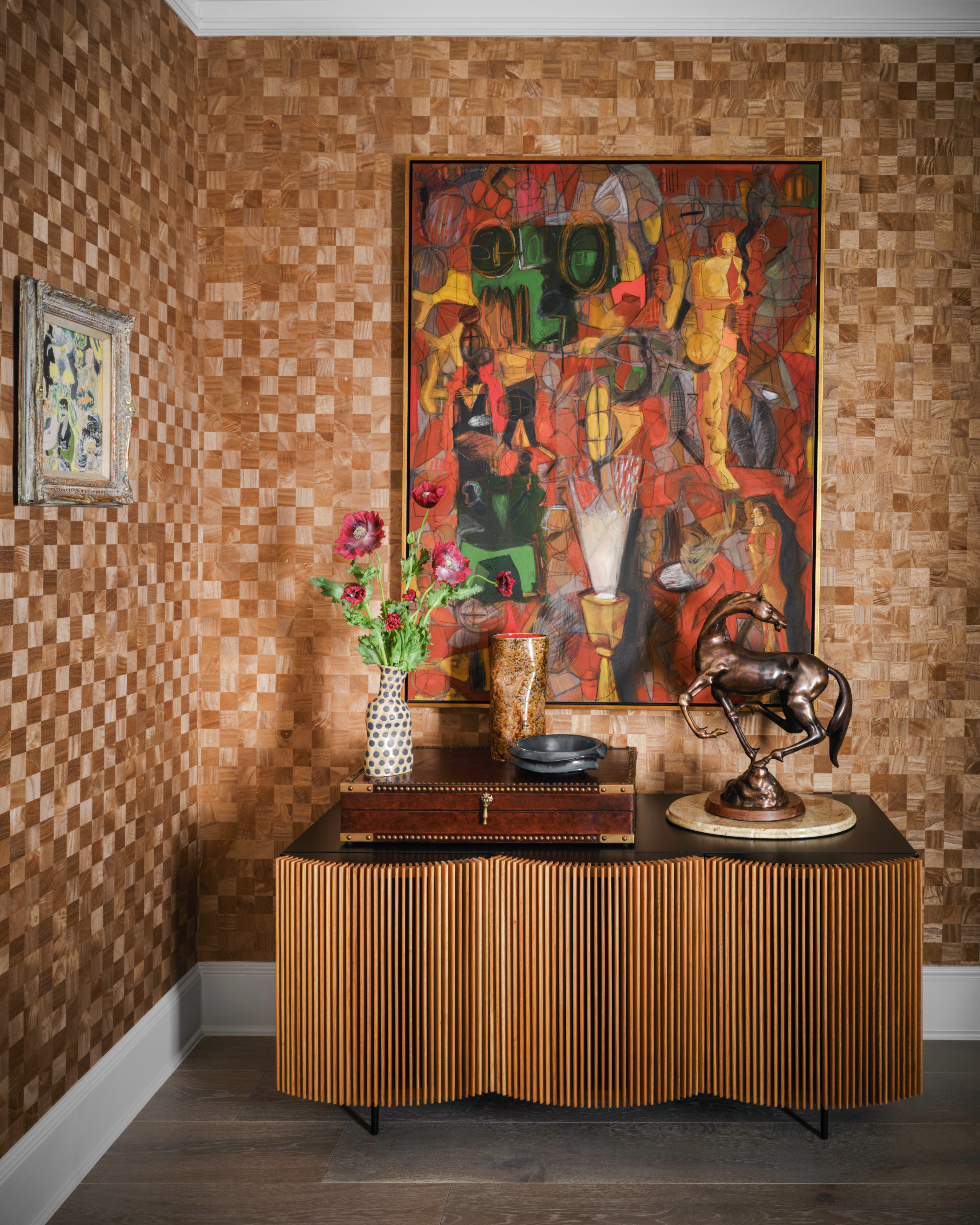 Corner of a room with checkered brown wallpaper, abstract artwork, ribbed wood sideboard with antique horse sculpture