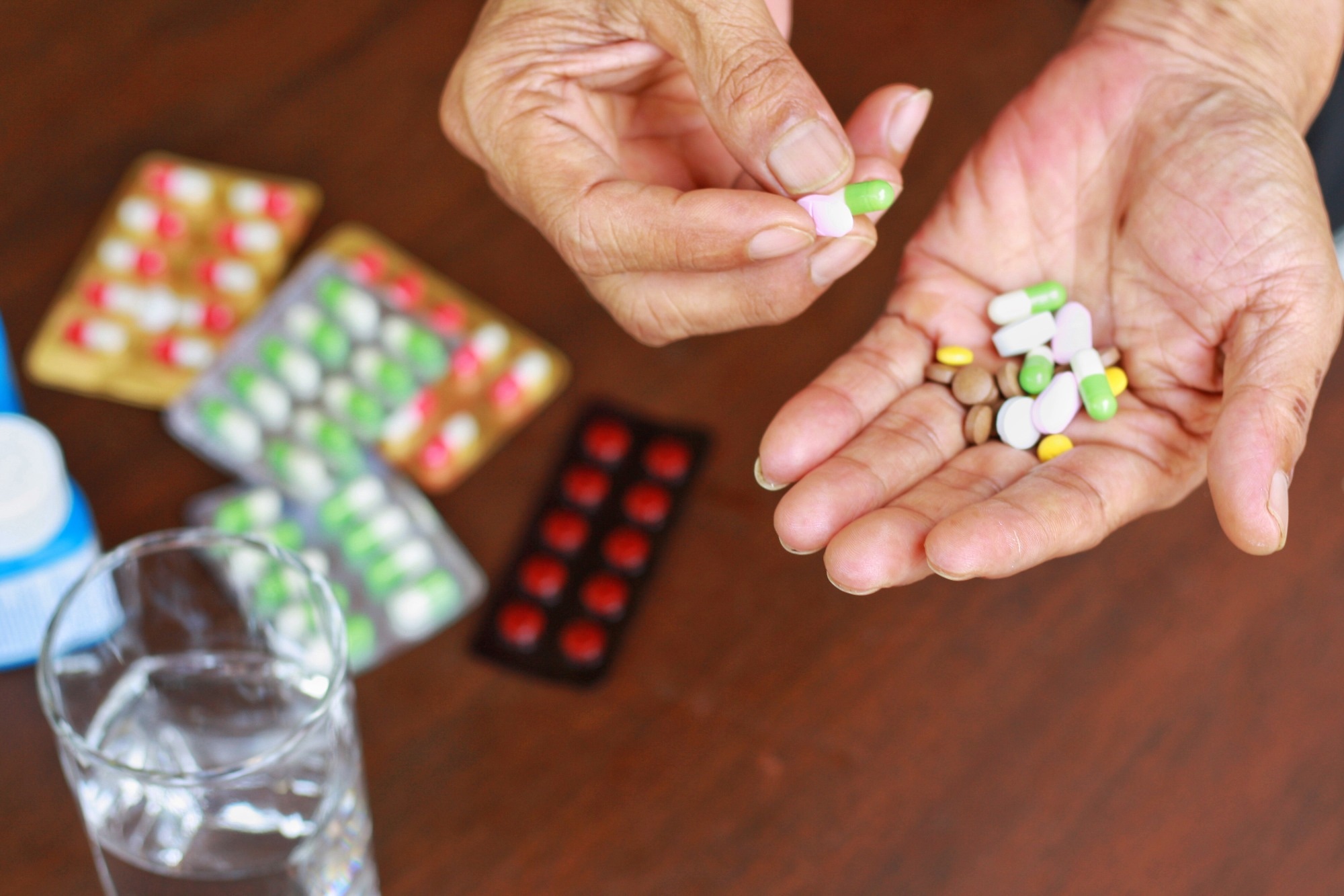 Elderly man hands holding many pills(tablet and capsule). Packets of mediation and glass of water