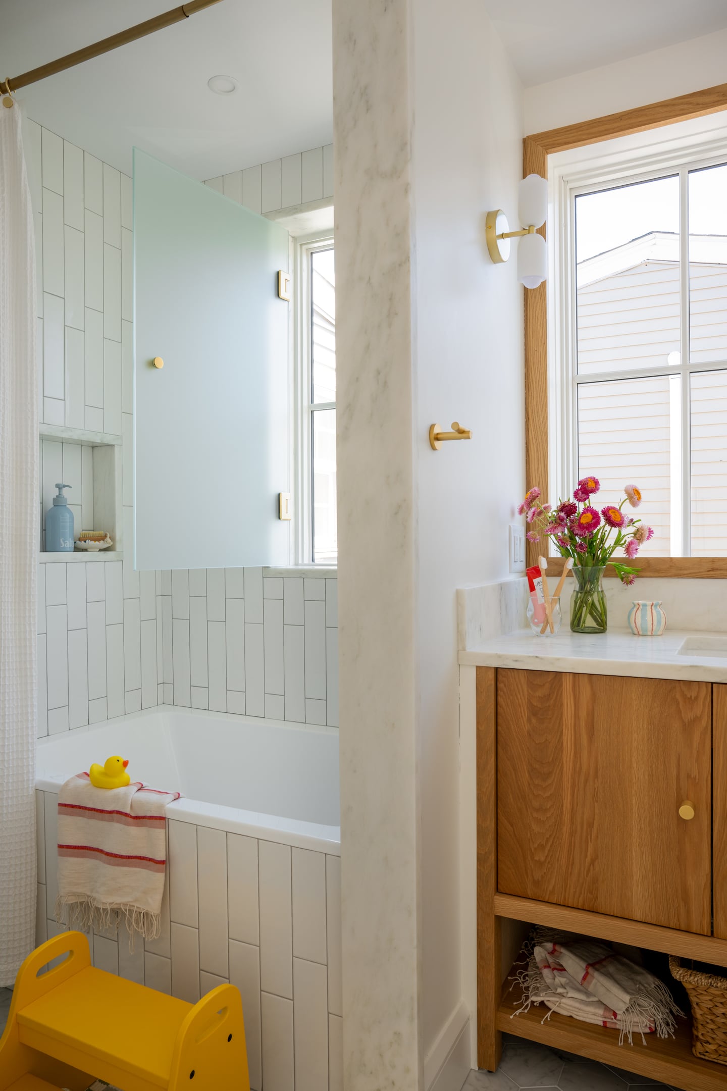 A section of a bathroom with a small tub set in an alcove with a window. On the right, there is built-in storage and another window.