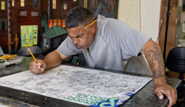 Black man leans over detailed drawing in art studio