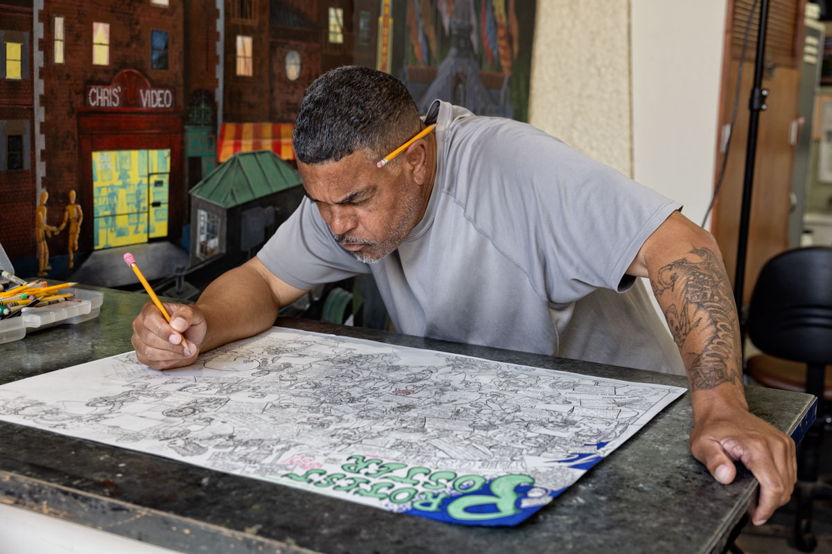 Black man leans over detailed drawing in art studio