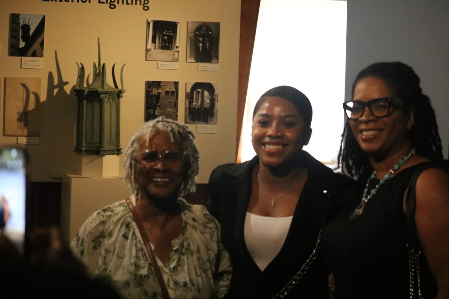 Jayla Trenyce (center) is all smiles on June 27, 2026, posing for a photo at the opening reception for her photography exhibit at the Ellwood House Museum in DeKalb.
