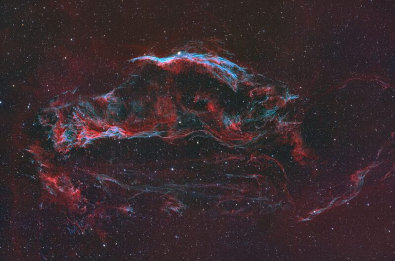 Large, arc-shaped clouds of gas in blue and red, with dark areas and numerous background stars.
