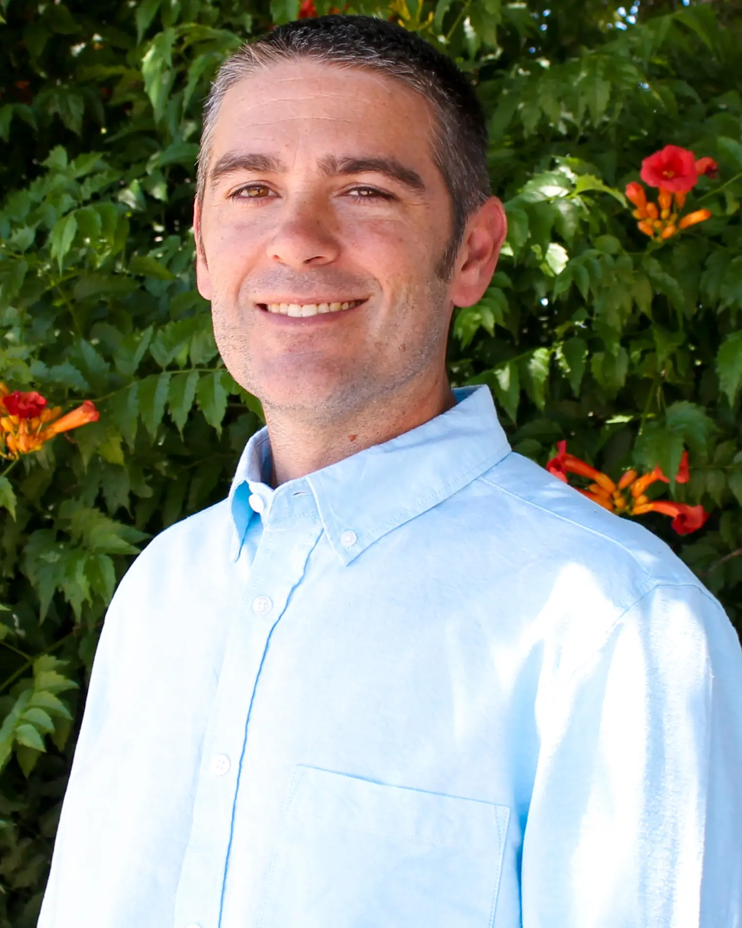 Portrait of a man in a collared shirt with a background of leaves and orange trumpet flowers