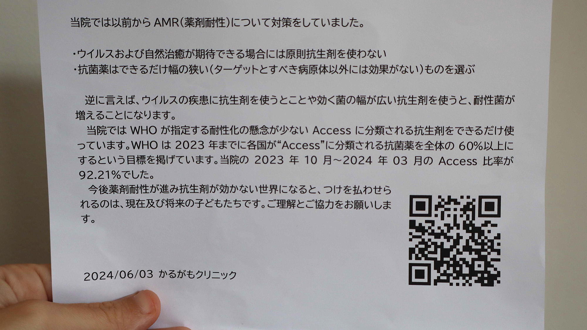 A person holds a piece of paper with Japanese writing on it and a QR code