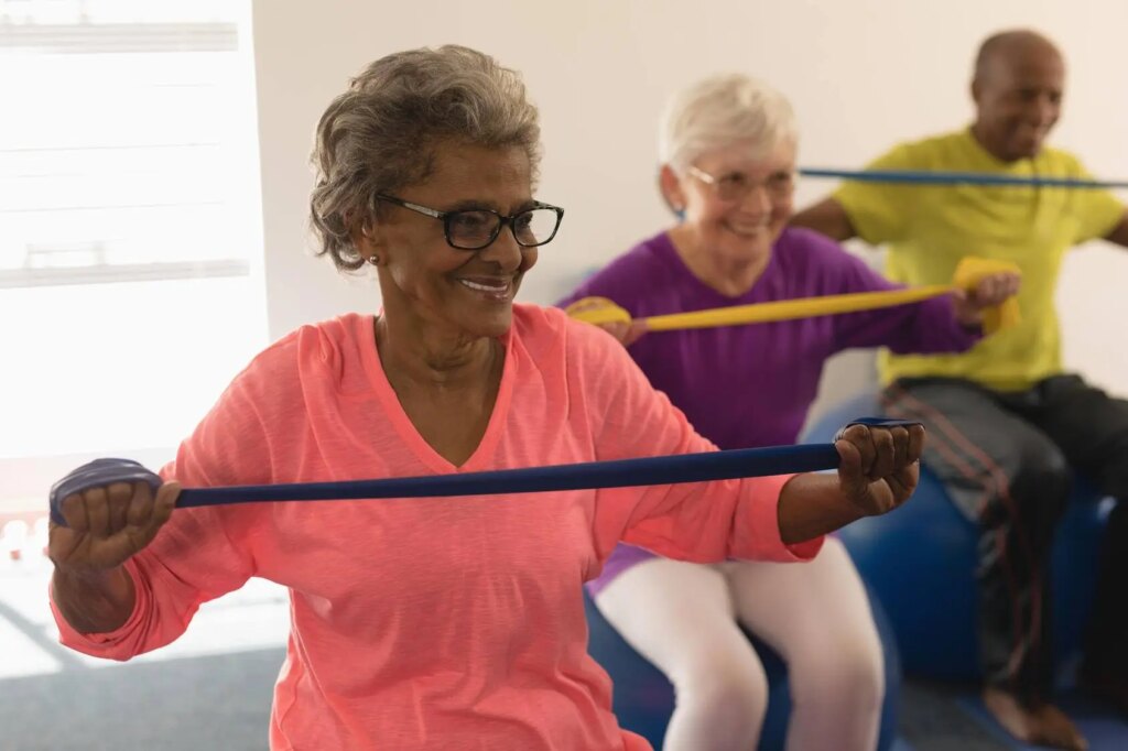 Three older people exercise together using resistance bands and exercise balls.