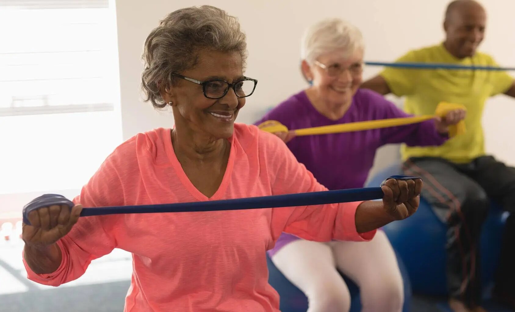 Three older people exercise together using resistance bands and exercise balls.
