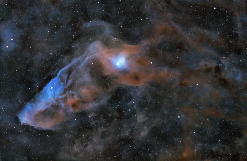 Large patch of bright bluish nebulosity, with smaller patches around and numerous background stars.