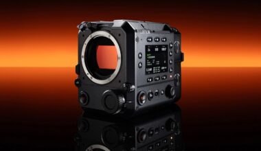 A black Fujifilm digital cinema camera body is displayed on a reflective surface with an orange to black gradient background. The camera features multiple dials, buttons, and a digital screen on its side.