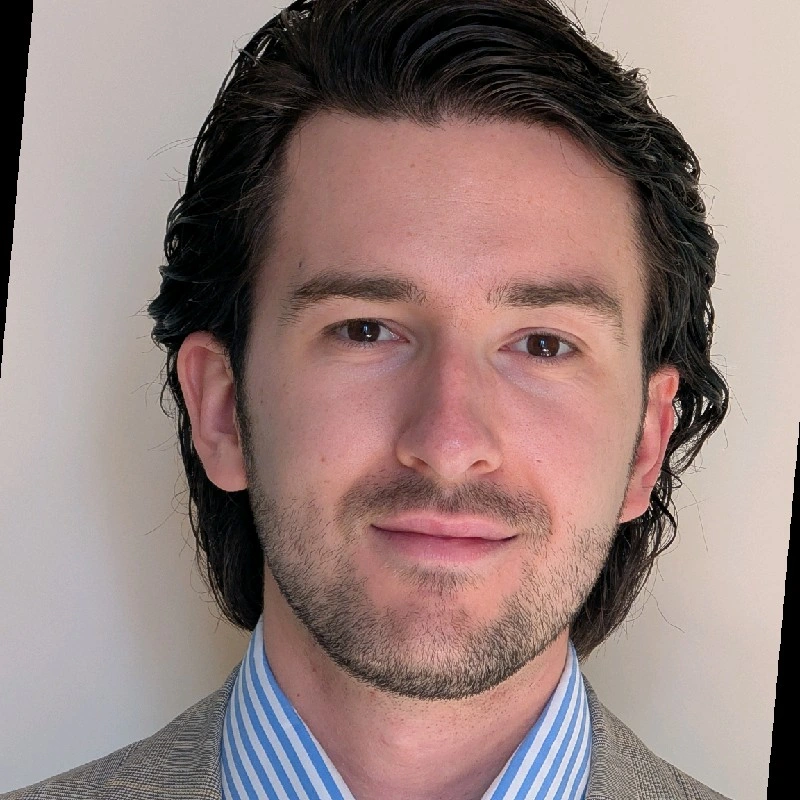 Smiling young man with dark hair and stubbly beard and mustache.