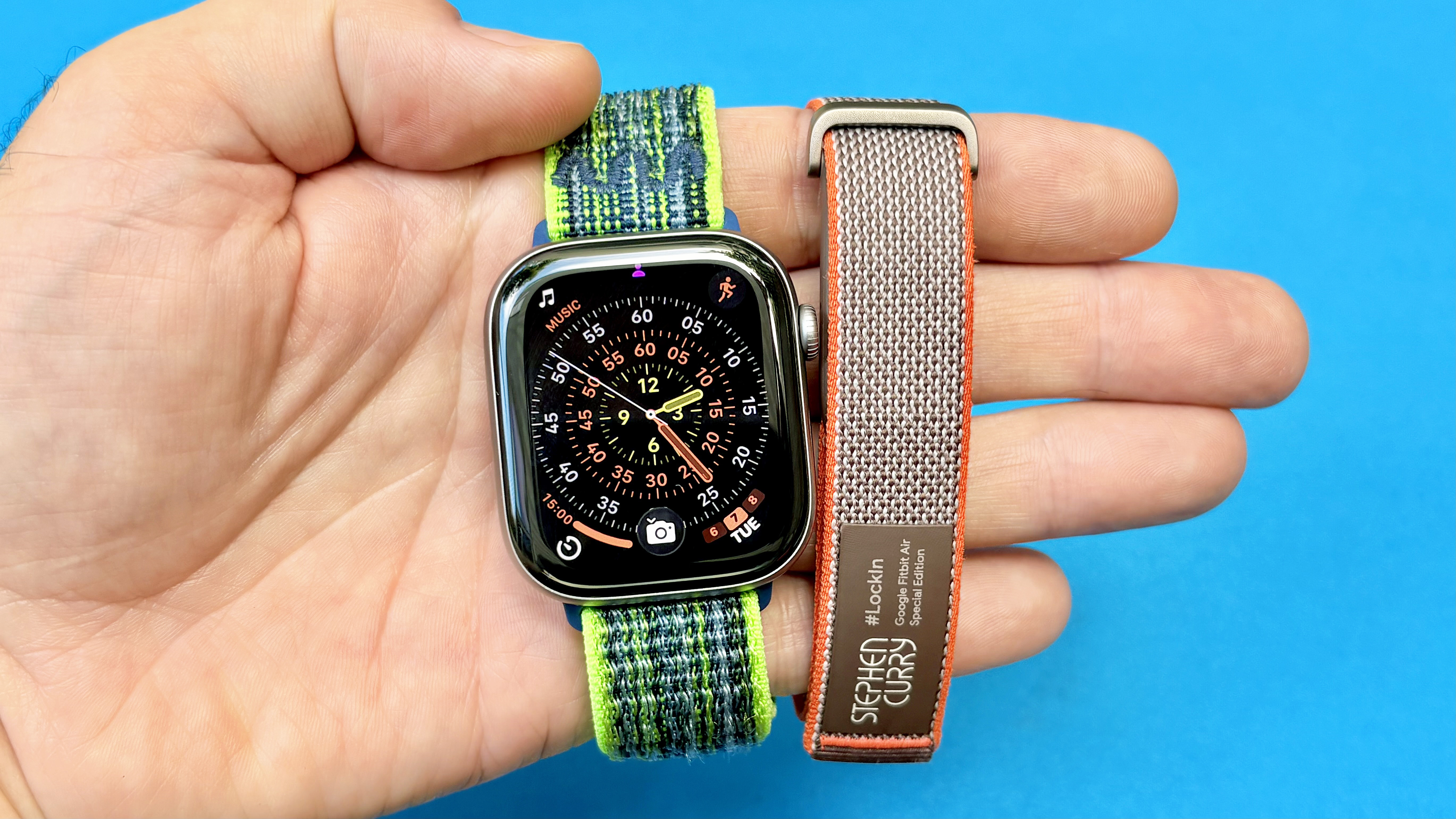 Close-up of the Apple Watch Series 11 next to the Fitbit Air; both are on colorful straps