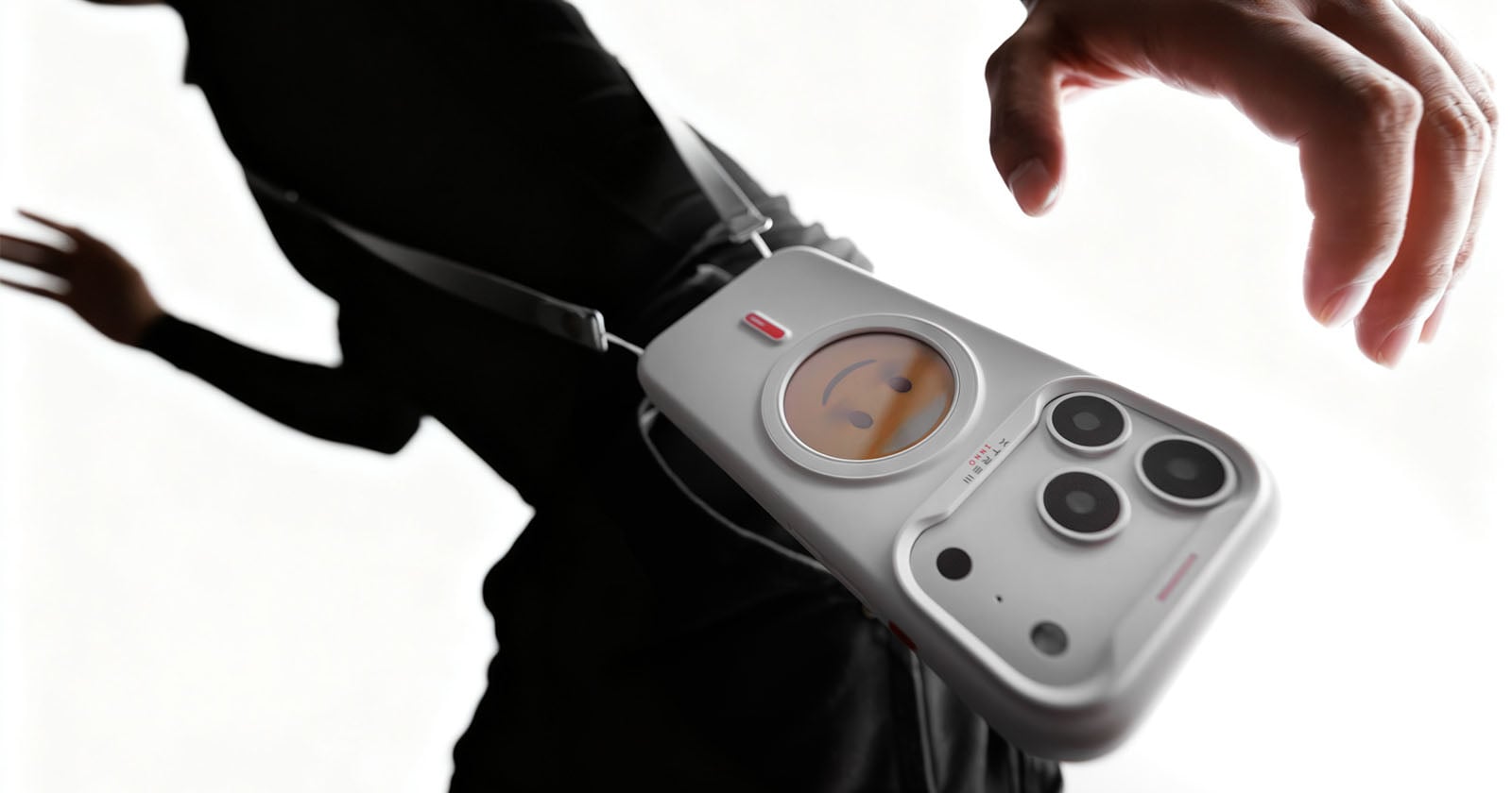 A person wearing black carries a white crossbody bag shaped like a smartphone with camera lenses and a small round screen displaying a cartoon face.