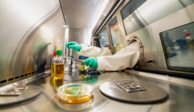 gloved hands reach into a sterile lab environment to work with chemicals.