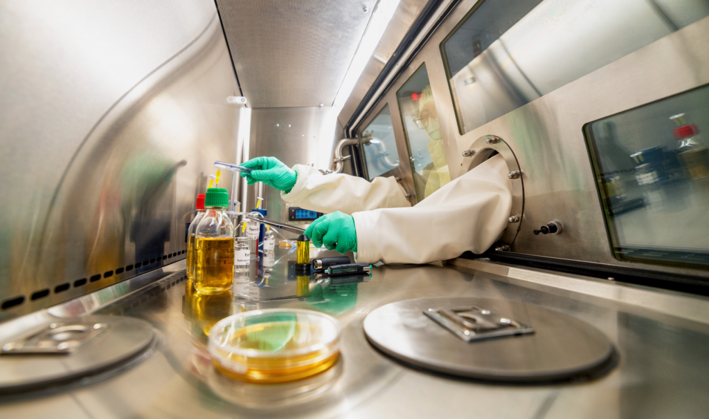 gloved hands reach into a sterile lab environment to work with chemicals.