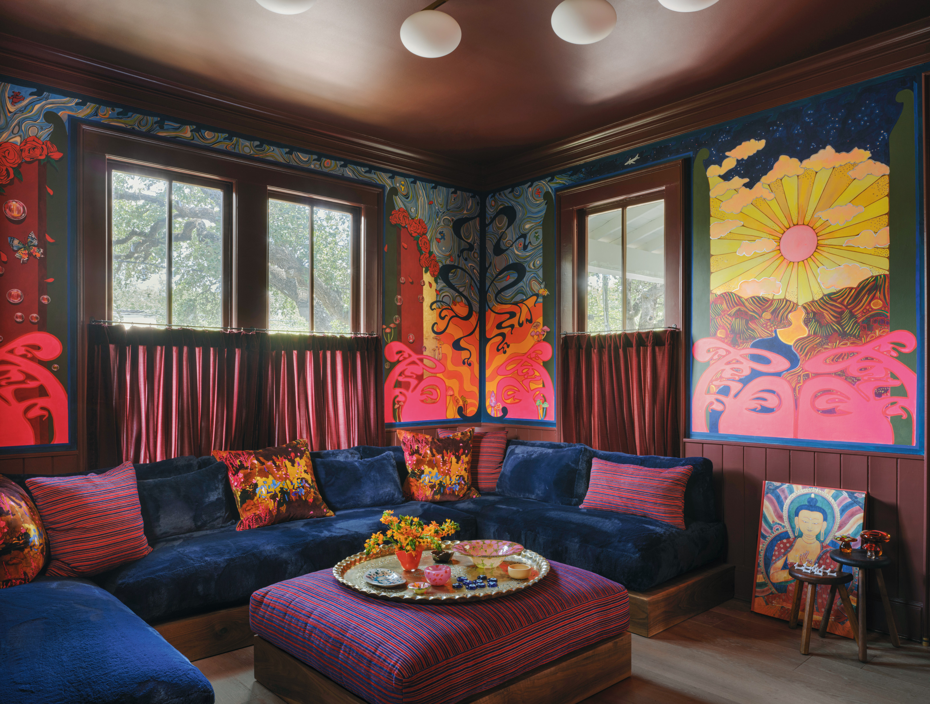 Snug with blue and pink walls, blue velvet U-shaped sofa, purple upholstered ottoman and psychedelic artwork