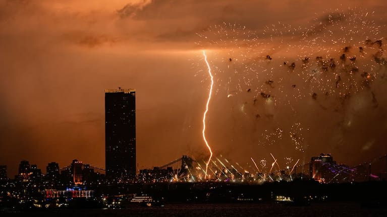A bolt of lighting strikes as fireworks are set off of the Brooklyn Bridge, as seen from Bayonne, New Jersey.
