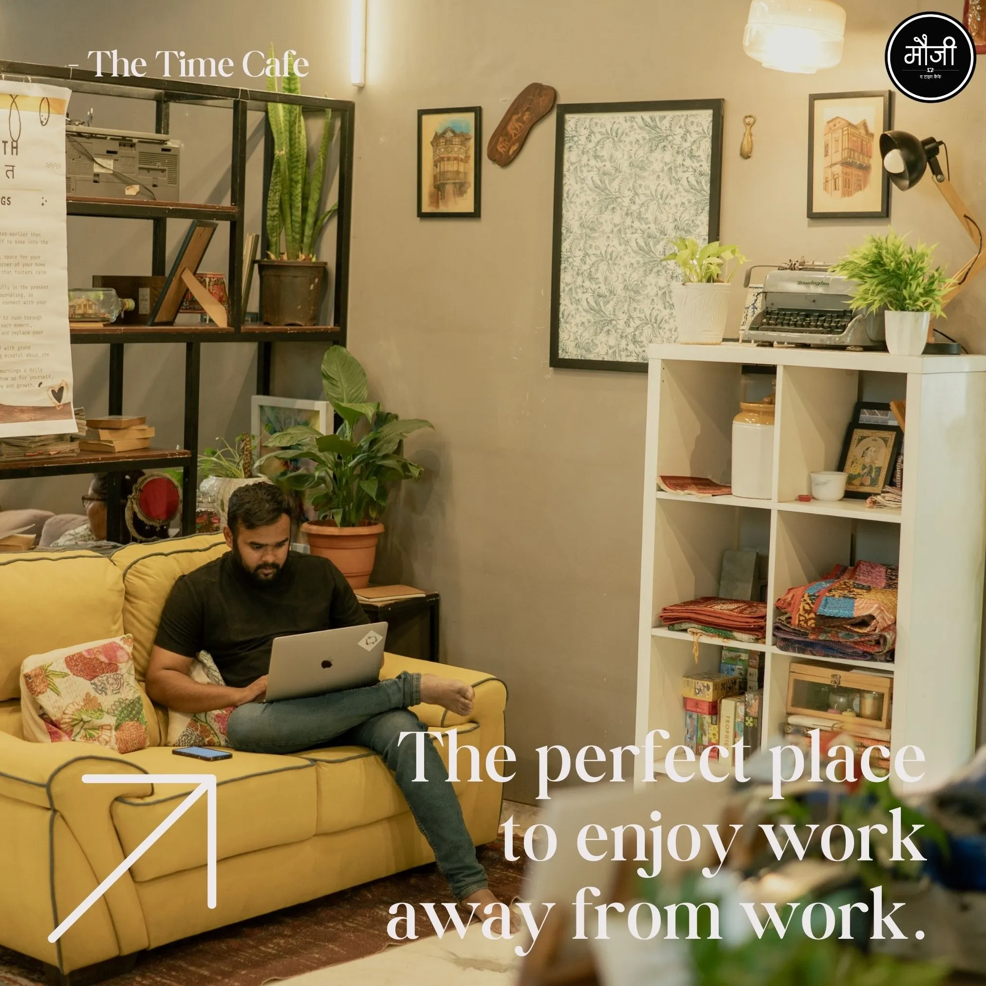 A person works on a laptop while sitting on a yellow sofa inside Mauji Time Cafe