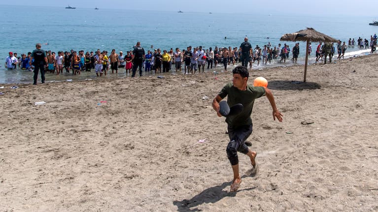 A migrant runs from Spanish police officers as they cordon off access to the beach for people crossing from Morocco into the Spanish enclave of Ceuta, Friday, July 31, 2026.