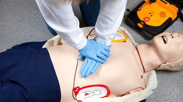 A person performs CPR and uses an AED on a dummy.