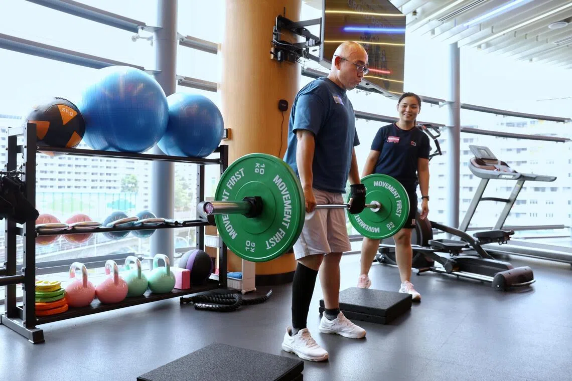 Stroke survivor Edmond Poh (left) using an assistive hand grip on his left hand while lifting weights under the watchful eyes of Exercise trainer Reosherra Lim. A year ago, he was could not have done this as he still needed a cane while walking.