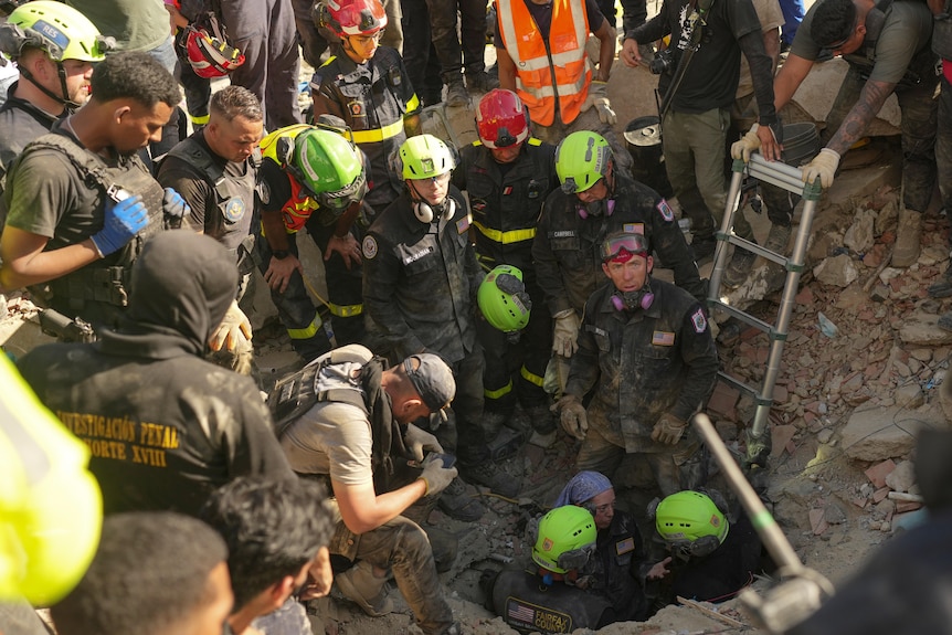 A group of search and rescue personnal stand over a hole in rubble after an earthquake.