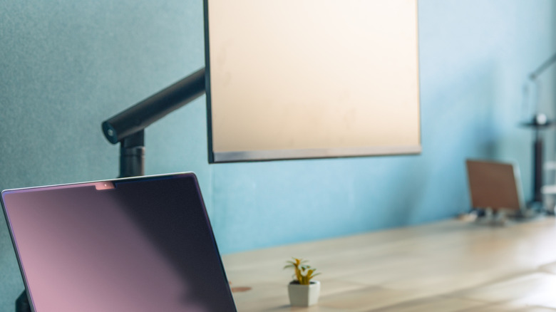 A home office desk with an open laptop and a monitor mounted on a monitor arm.