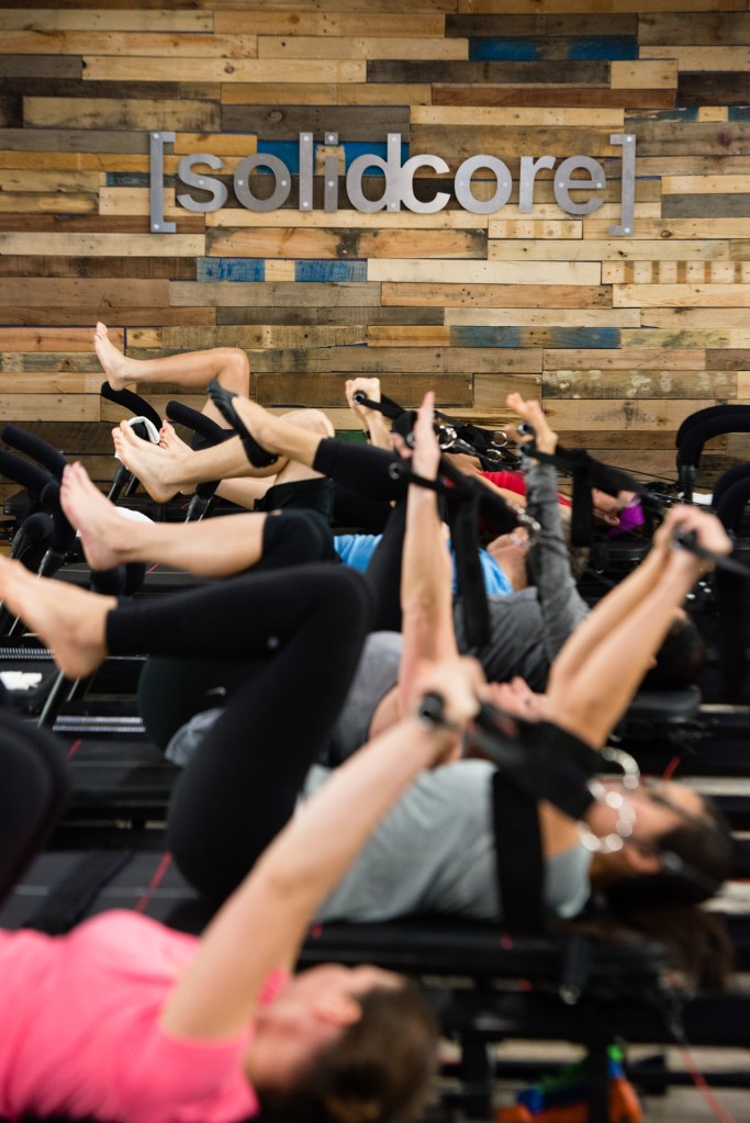 People exercising on fitness equipment at Solidcore studio.