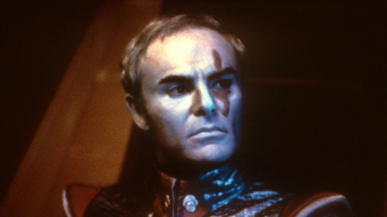 Sador (John Saxon) standing in a dark room in 
