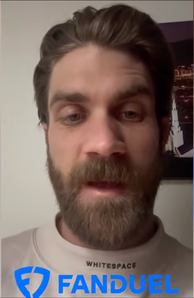 Bryce Harper with a beard wearing a white sweatshirt and a FanDuel logo.