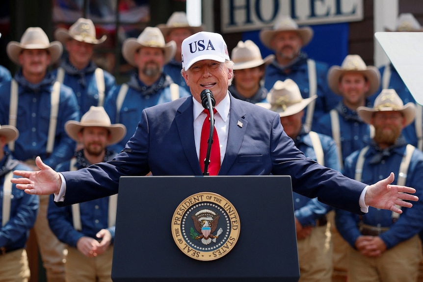 US President Donald Trump speaks at Burning Hills Amphitheatre with his hands outstretched.