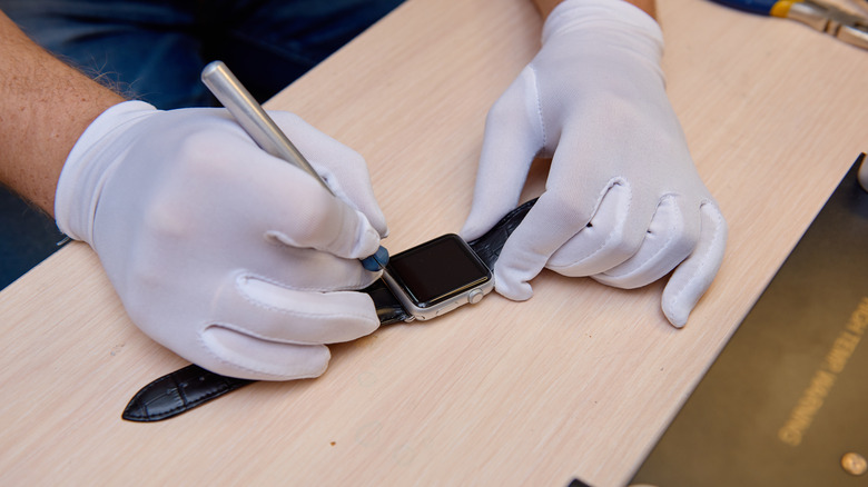 A person wearing white gloves repairing a smartwatch.