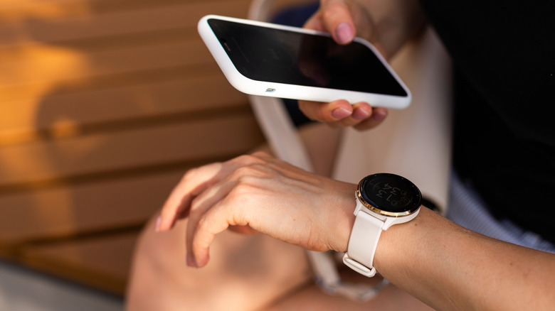 A woman holding a phone and looking at a round smartwatch.
