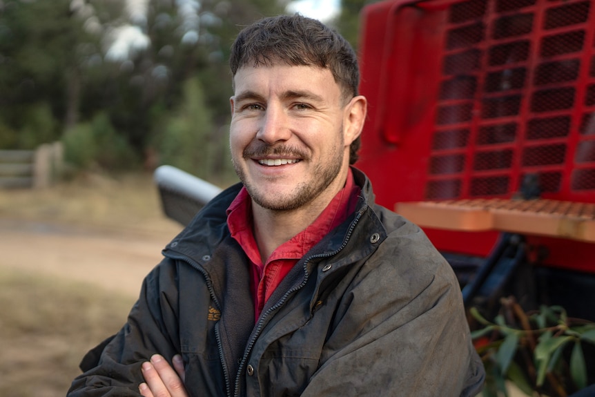A man with a big smile. He wears a black jacket and a red shirt.