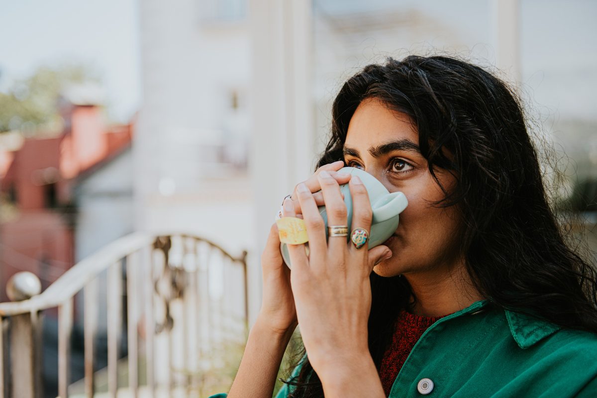A woman cups her hands around a mug and drinks the brew