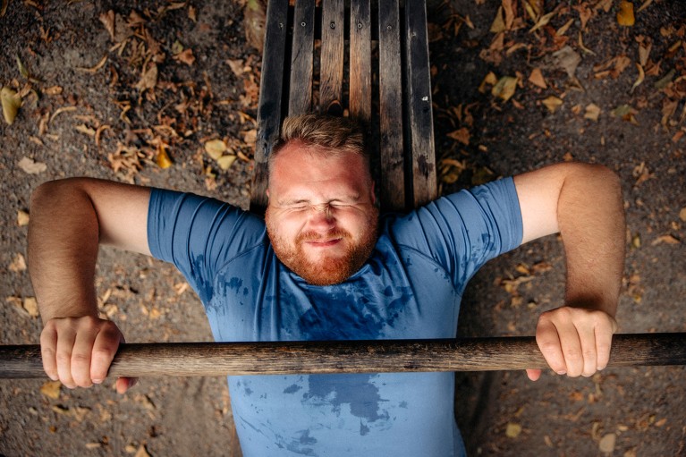 View from above of a man at full exertion, doing a bench press at an outdoor gym.