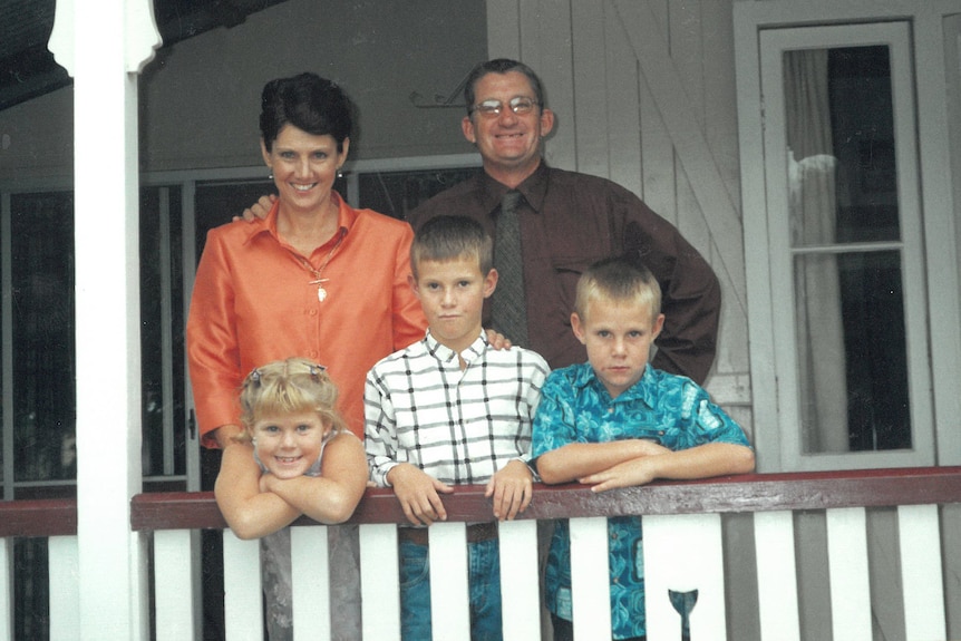 A family stands on the porch of a big house for a family photo.