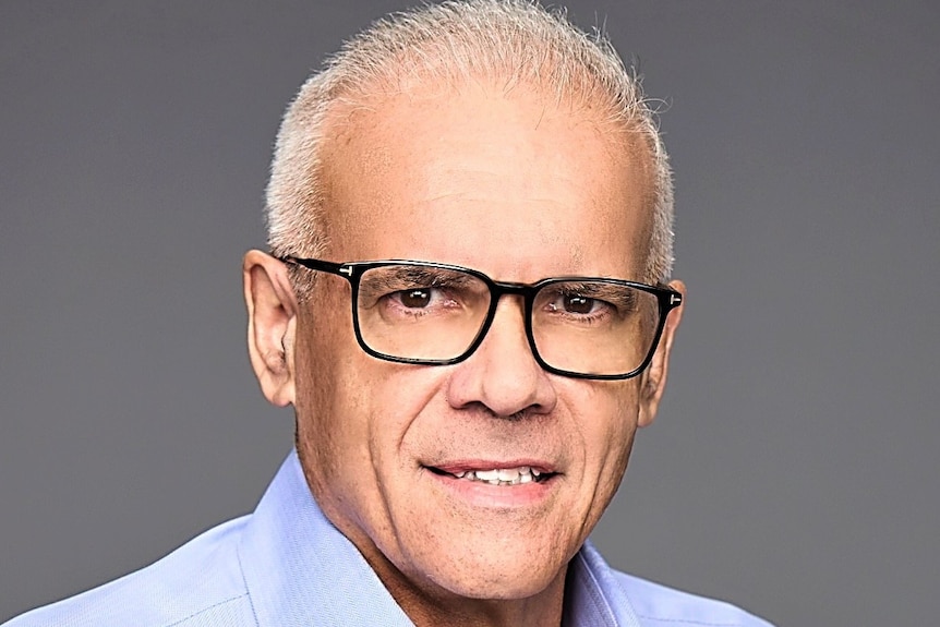 man with dark glasses smiling in blur shirt grey background