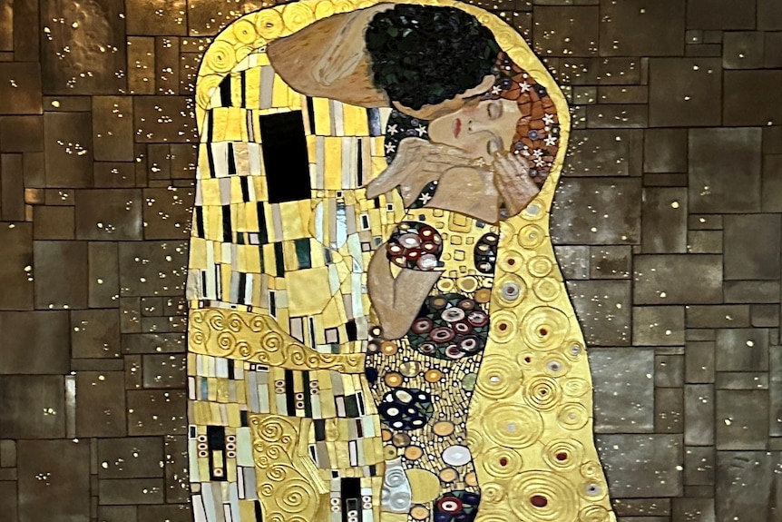 close up of gold mural of a man holding a woman's face with her eyes closed.