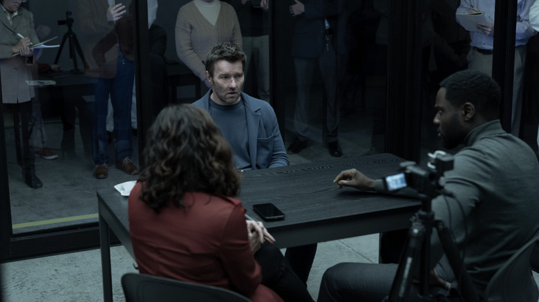 Joel Edgerton as Jason Dessen in Dark Matter, being interviewed at a black table in a glass room.
