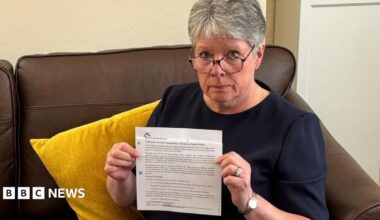 Alison Williams, a woman in her mid-60s with short, grey hair, holding a letter from the Civil Service Pensions Scheme informing her of delays to pension payments.