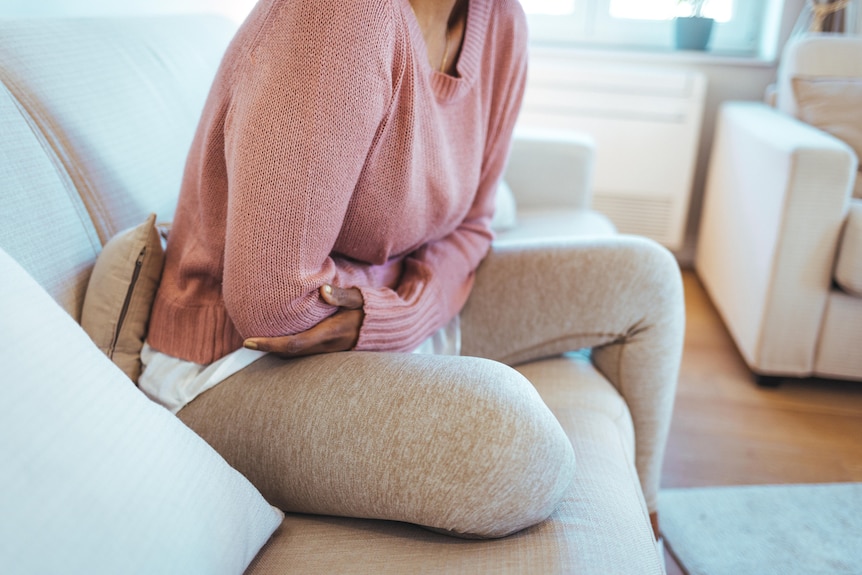 Woman holds her stomach while sitting on couch.