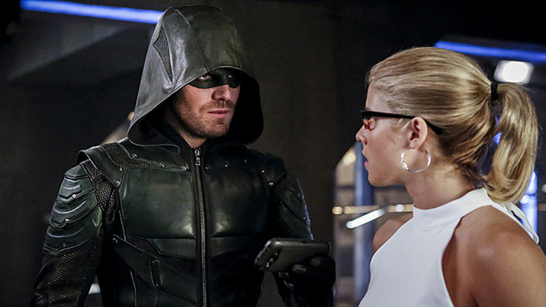 The Green Arrow, holding a phone, stands beside Felicity Smoak in the Arrowcave on The CW's Arrow.